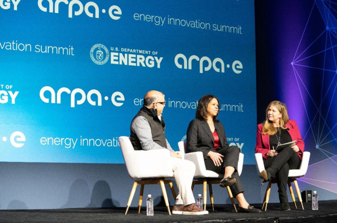 Kathi Vidal speaks on a conference stage, sitting with two other people, with logo for the ARPA-E energy innovation summit in the background