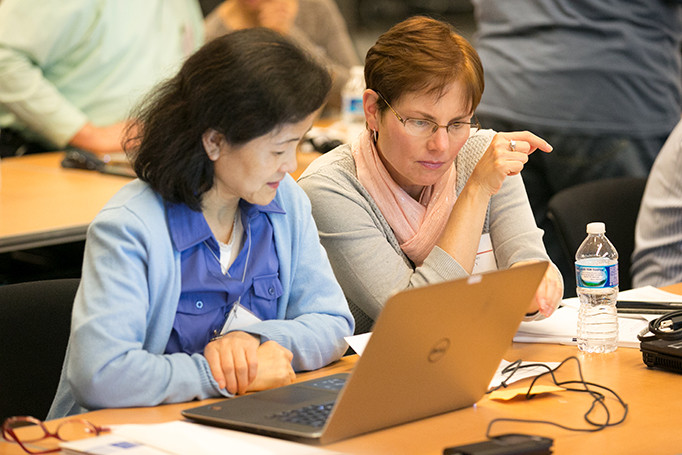 Two women sitting together with their attention drawn to a piece of paper and laptop screen