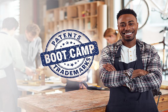 Man poses with his arms crossed in a woodshop beside a "Patent and Trademarks Bootcamp" logo 